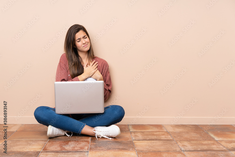 Teenager student girl sitting on the floor with a laptop having a pain in the heart Teenager student girl sitting on the floor with a laptop having a pain in the heart