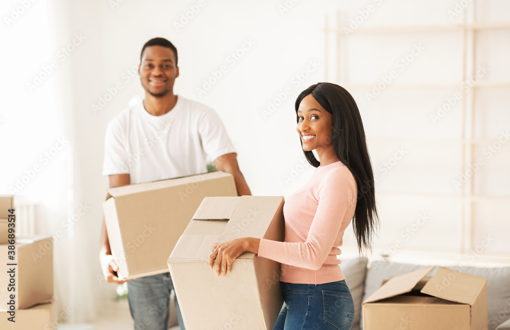 Moving into new home. Happy black guy and his beautiful girlfriend with boxes posing and smiling during relocation - obrazy, fototapety, plakaty 