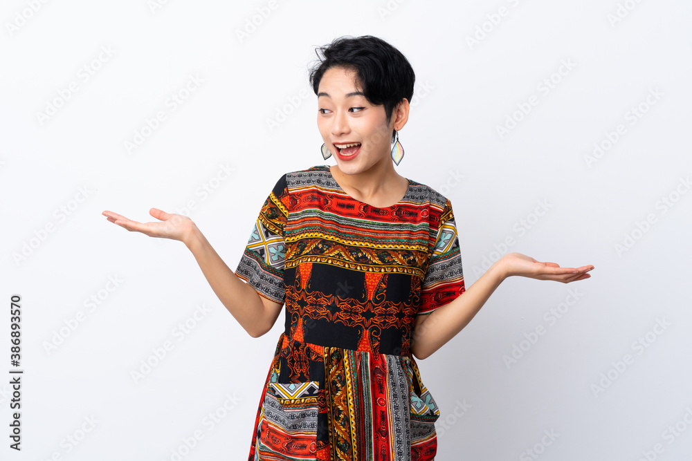Young Asian girl with a colorful dress over isolated white background holding copyspace with two hands Young Asian girl with a colorful dress over isolated white background holding copyspace with two hands