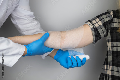 The traumatologist puts a bandage on the elbow of the female patient. The concept of help with fractures and sprains. The technique of applying a cruciform bandage. photo