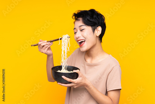 Photographie Young Asian girl over isolated yellow background holding a bowl of noodles with