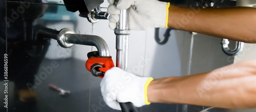 Plumber fixing white sink pipe with adjustable wrench.