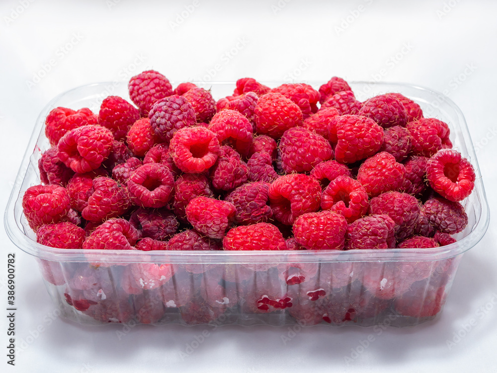 Naklejka premium Plastic bowl of ripe red raspberries on a white background