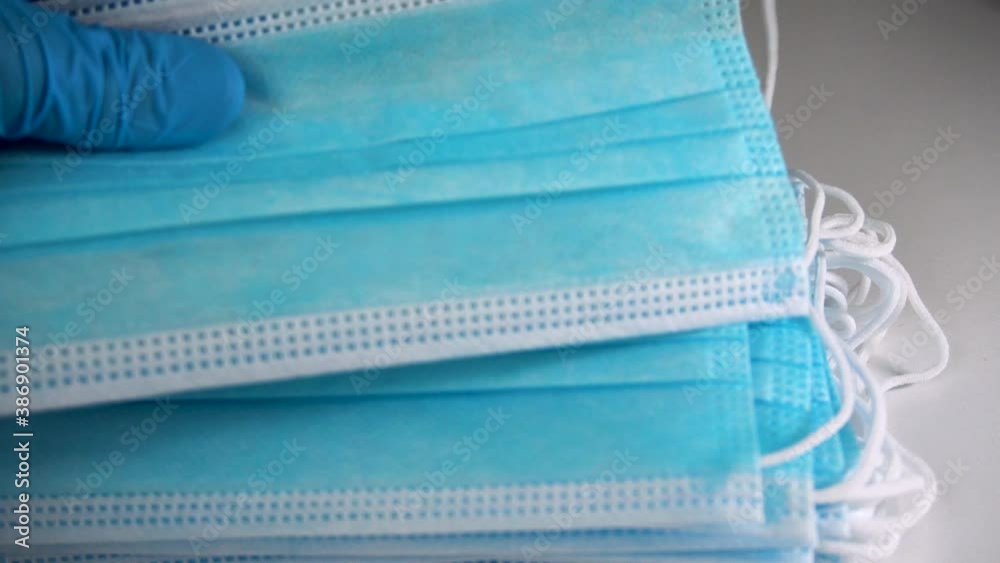 Hands wear blue medical gloves holds surgical face mask on blue background. Pandemic concept. Prevent the spread of virus disease. Doctor holds surgical mask in hospital. Mounting face mask correctly