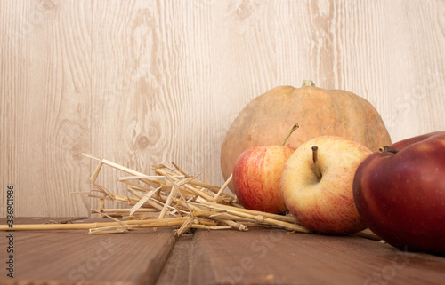 Orange pumpkin on the hay next to three red apples on a dark wooden background. autumn mood. photo