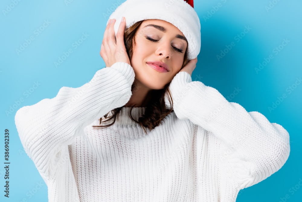 young brunette woman with closed eyes touching hat on blue young brunette woman with closed eyes touching hat on blue