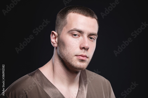 Studio portrait in low key manly attractive male physiotherapist massage therapist in contrast light in overalls on a black background