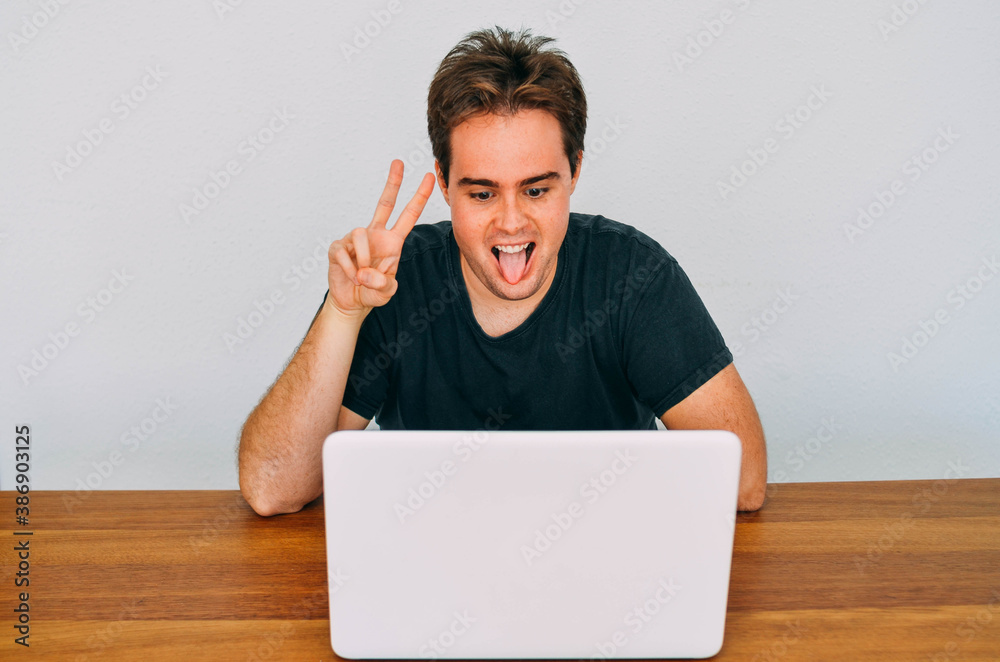 Young Flabby Redhead Nerd Sticking Out Tongue Posing Victory Symbol to his Laptop Screen in Video Call Young Flabby Redhead Nerd Sticking Out Tongue Posing Victory Symbol to his Laptop Screen in Video Call