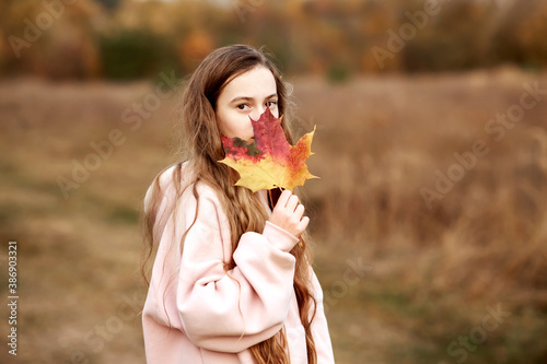 Portrait of a teenage girl with long hair holding a maple leaf near her face.