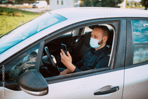 Portrait of a businessman with a protective mask holding a phone in his hand while sitting in a car. Business conversation on the way to work during the pandemic COVID - 19 coronavirus © Dragica