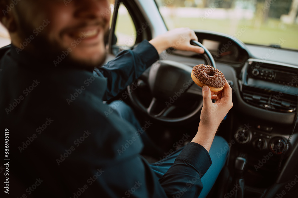 A close - up of hand of a young caucasian businessman holding a delicious chocolate doughnut and driving a car on the way to work. A sweet meal in transport A close - up of hand of a young caucasian businessman holding a delicious chocolate doughnut and driving a car on the way to work. A sweet meal in transport