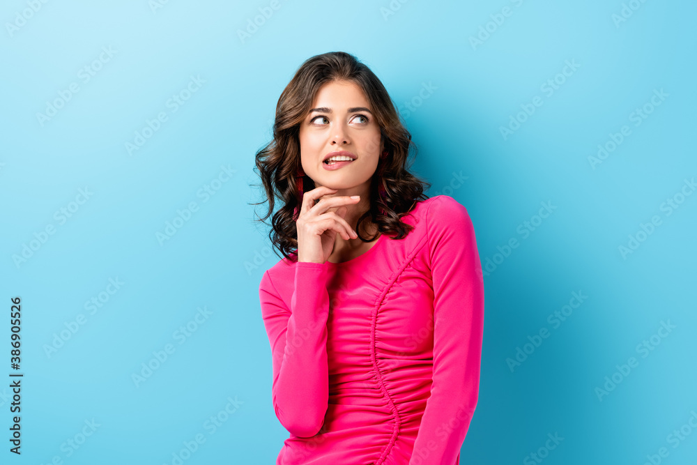 pensive young woman biting lips and looking away on blue pensive young woman biting lips and looking away on blue