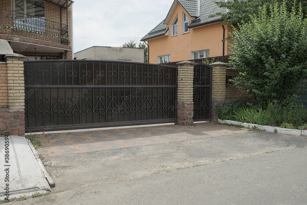 one black metal gates a forged pattern and part of a brick brown fence on the street one black metal gates a forged pattern and part of a brick brown fence on the street