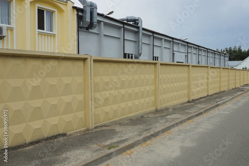Wallpaper Mural a long yellow concrete fence by an asphalt road in front of an industrial wall of a factory Torontodigital.ca