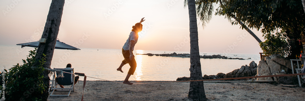 Girl goes on slackline at sunset on a tropical beach
