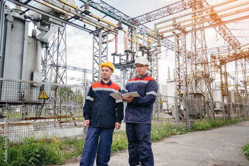 Two specialist electrical substation engineers inspect modern high-voltage equipment in the evening. Energy. Industry