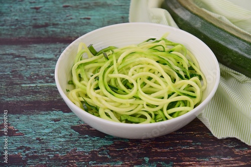 Zoodles (zucchini noodles) in a bowl on wooden background