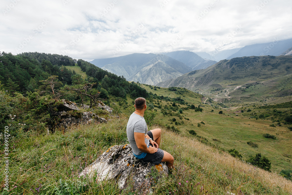 A young man sits and enjoys a stunning view of the beautiful mountains while traveling. Wildlife