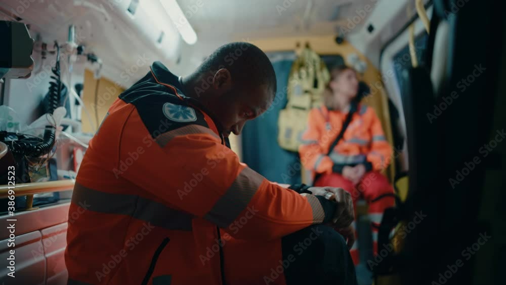Tired Black African American Paramedic Tries to Rest in an Ambulance Vehicle Going for Emergency. Emergency Medical Technicians are on Their Way to a Call Outside the Healthcare Hospital. Tired Black African American Paramedic Tries to Rest in an Ambulance Vehicle Going for Emergency. Emergency Medical Technicians are on Their Way to a Call Outside the Healthcare Hospital.