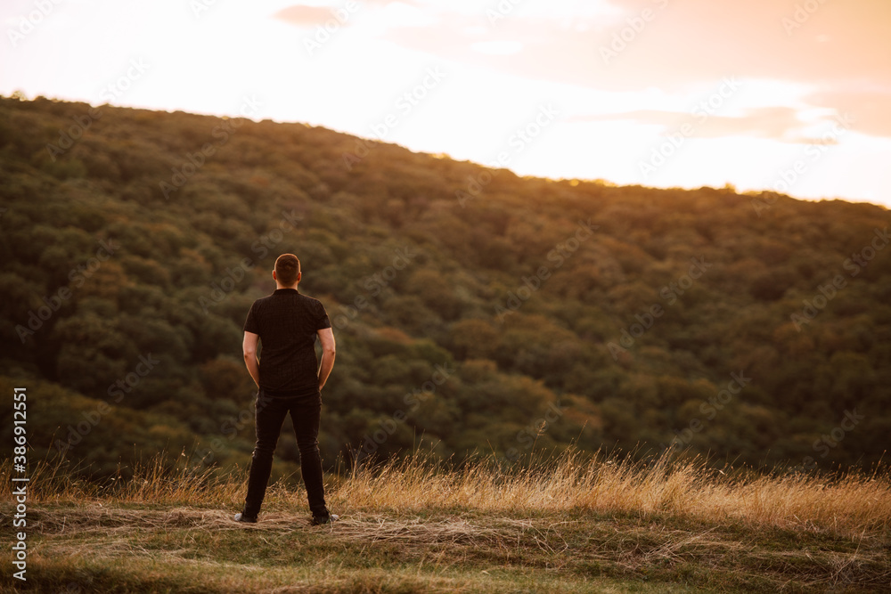 Back view of  a young caucasian man standing on a mountain at sunset. A beautiful day in the fresh mountain air