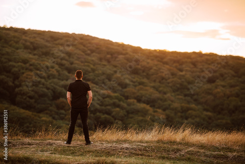 Back view of a young caucasian man standing on a mountain at sunset. A beautiful day in the fresh mountain air