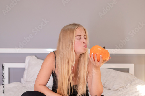 beautiful blonde with pumpkin in white bedroom. halloween concept.
