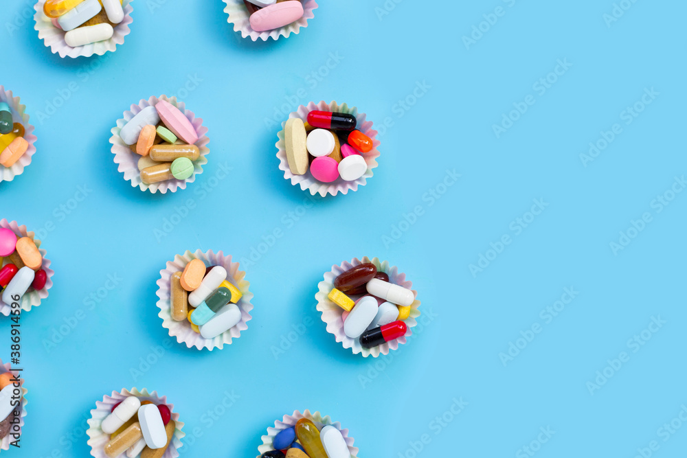 Colorful tablets with capsules and pills in cupcake wrappers on blue background. Colorful tablets with capsules and pills in cupcake wrappers on blue background.