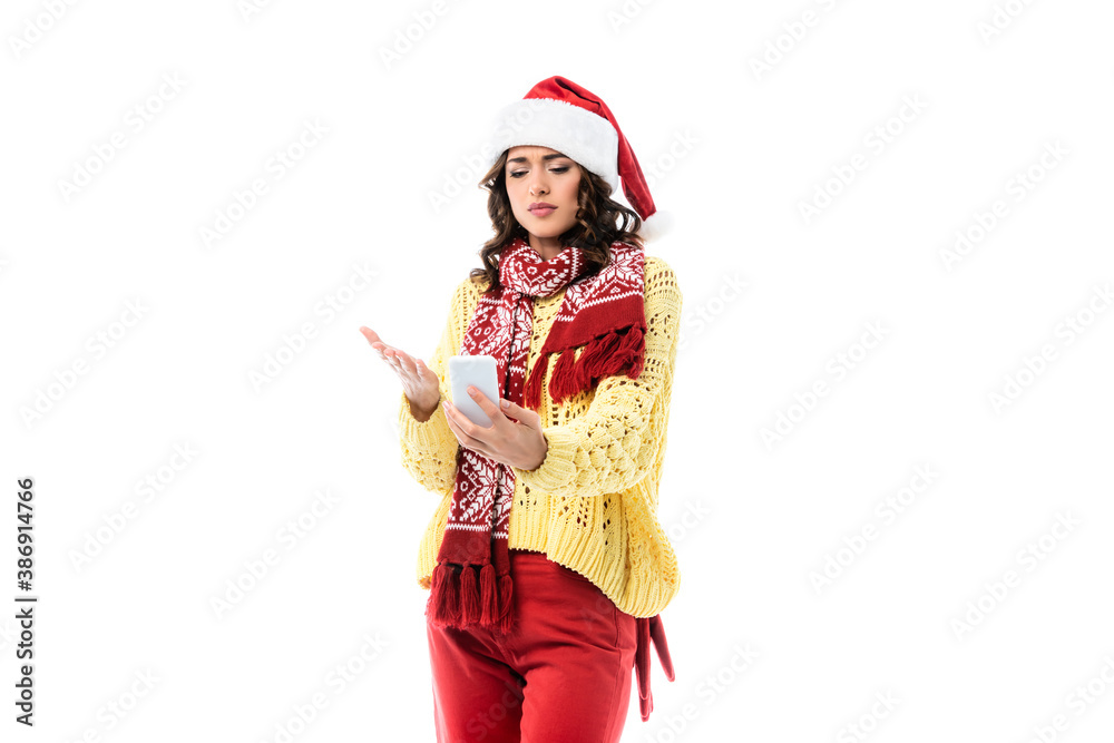young woman in santa hat and scarf pointing with hand while holding smartphone isolated on white young woman in santa hat and scarf pointing with hand while holding smartphone isolated on white