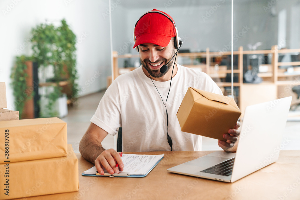 Male joyful delivery assistance working with packages and laptop Male joyful delivery assistance working with packages and laptop
