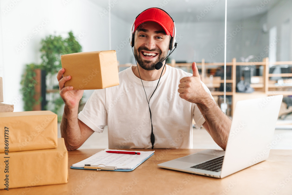 Male joyful delivery assistance working with packages and laptop