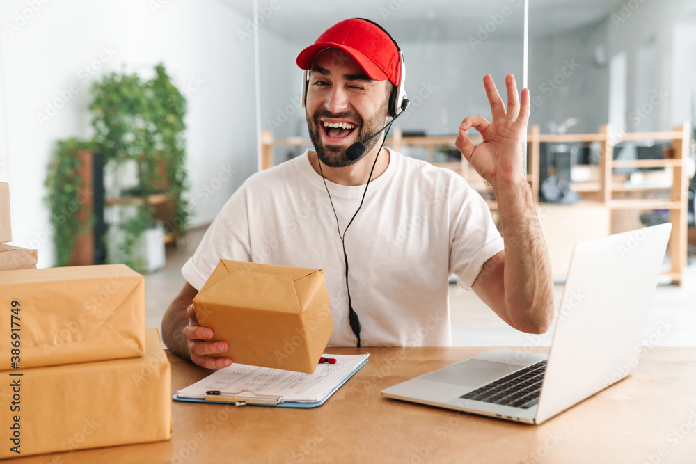 Male joyful delivery assistance working with packages and laptop Male joyful delivery assistance working with packages and laptop