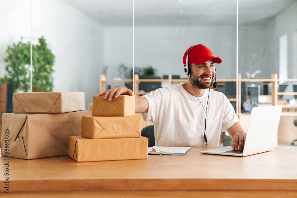 Male joyful delivery assistance working with packages and laptop Male joyful delivery assistance working with packages and laptop