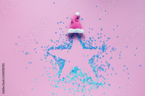 creative christmas concept: star shape made of blue mini stars in christmas hat on pink background