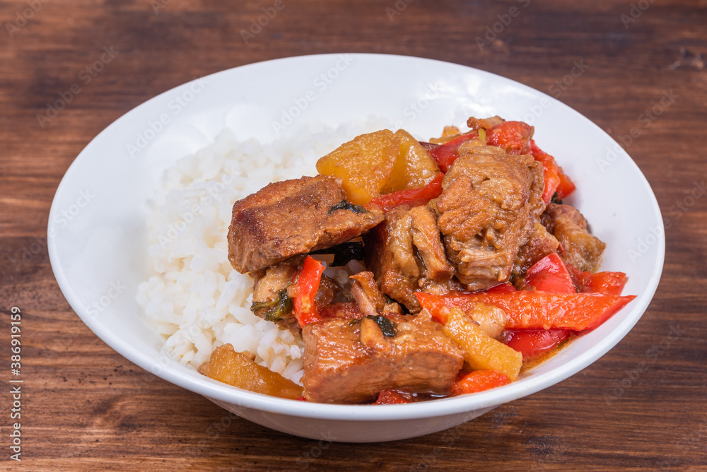 Adobo pork with pineapple and pepper in bowl with boiled rice on wooden dark background Adobo pork with pineapple and pepper in bowl with boiled rice on wooden dark background
