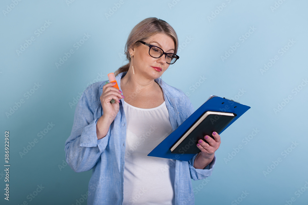 Senior caucasian woman is reading something while posing on a blue wall in glasses and holding some folders Senior caucasian woman is reading something while posing on a blue wall in glasses and holding some folders