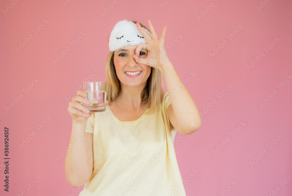 Woman in cute nightwear and sleep mask, looking coquettish with pleased tender smile, drinking water, start day healthy and active, standing pink background Woman in cute nightwear and sleep mask, looking coquettish with pleased tender smile, drinking water, start day healthy and active, standing pink background