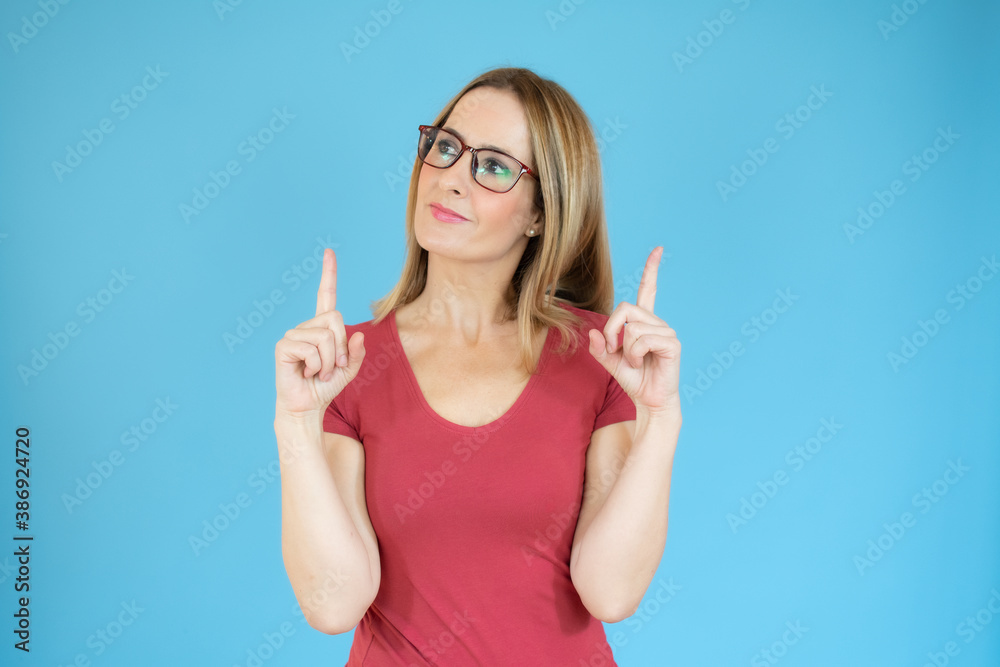 Fototapeta premium Portrait of beautiful young woman pointing up over blue background.