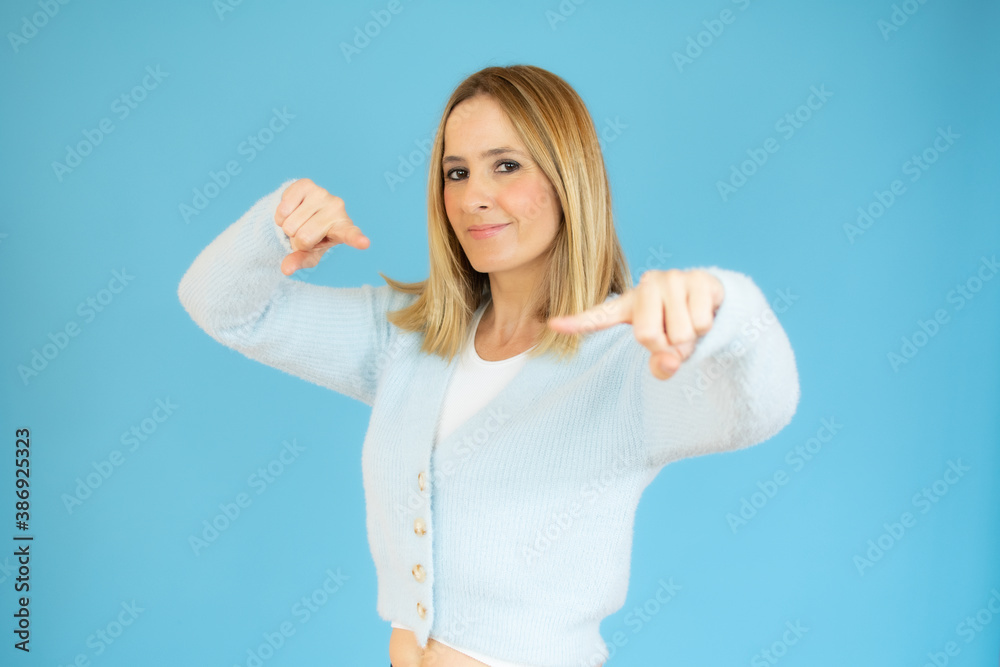 Fototapeta premium Portrait of attractive happy young woman pointing fingers over blue background.