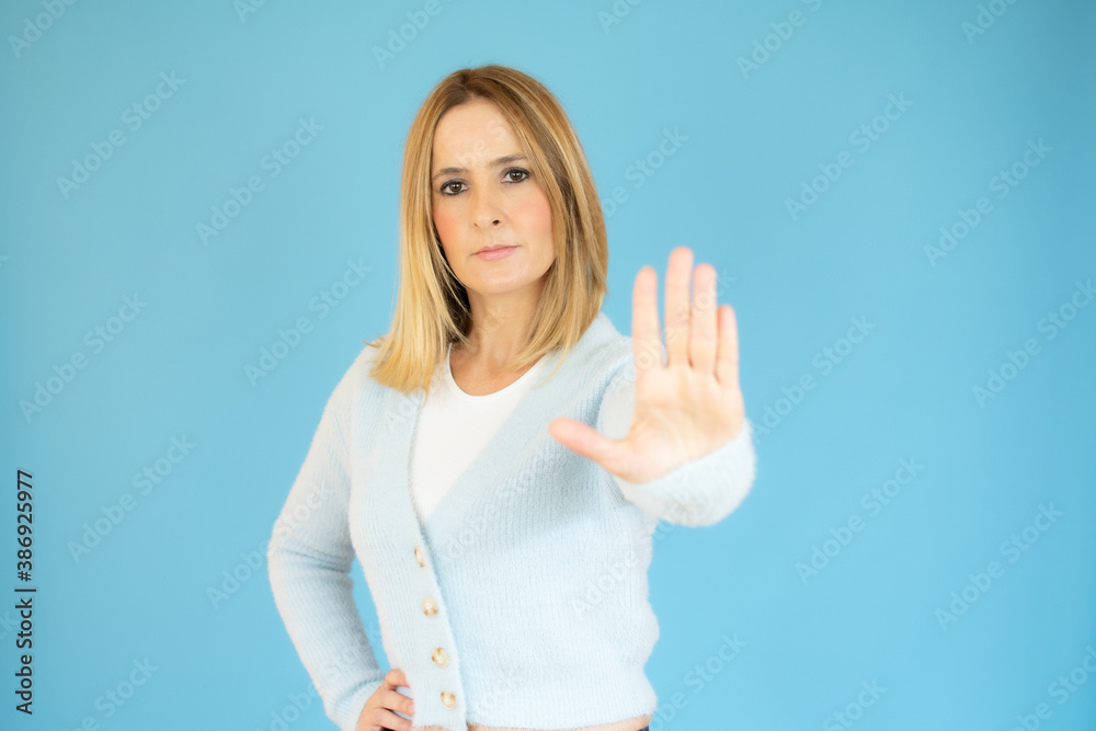 Fototapeta premium Young beautiful woman wearing casual blue sweater over blue background doing stop sing with palm of the hand. Warning expression with negative and serious gesture on the face.