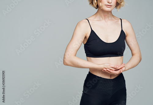 Tableau sur toile Woman in sportswear gesturing with her hands on a gray background and black legg