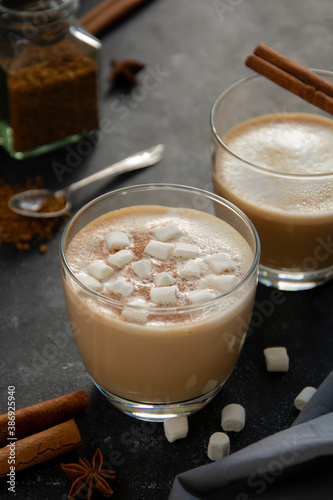 Hot chocolate with whipped cream in glass isolated with cinnamon stick, over dark background