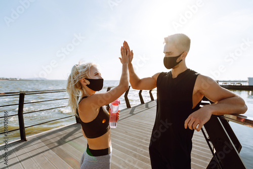 Young man and woman in protective masks running and doing exercises outdoors in the morning. Sport  Active life  Jogging during quarantine. Covid-19.