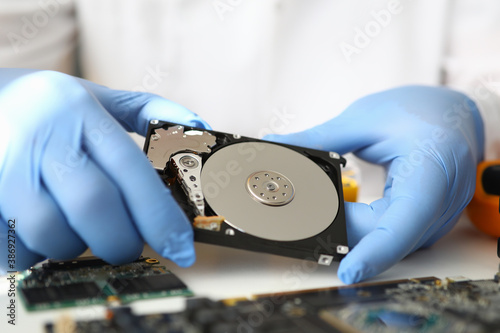 Gloved master holds hard drive away from computer. Computer repair service concept photo