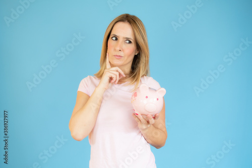 Portrait of a pensive casual woman holding an alarm clock looking away at copy space isolated over blue background