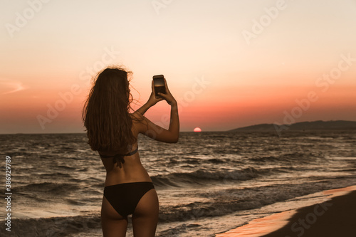 Fototapeta Naklejka Na Ścianę i Meble -  Woman taking photos of a sunset with a mobile phone