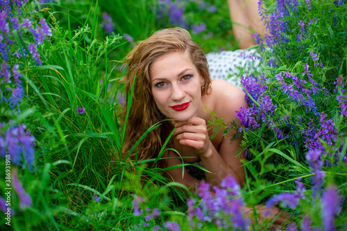 Beautiful young blonde girl in a green field among purple wildflowers. Wildlife beautiful girl