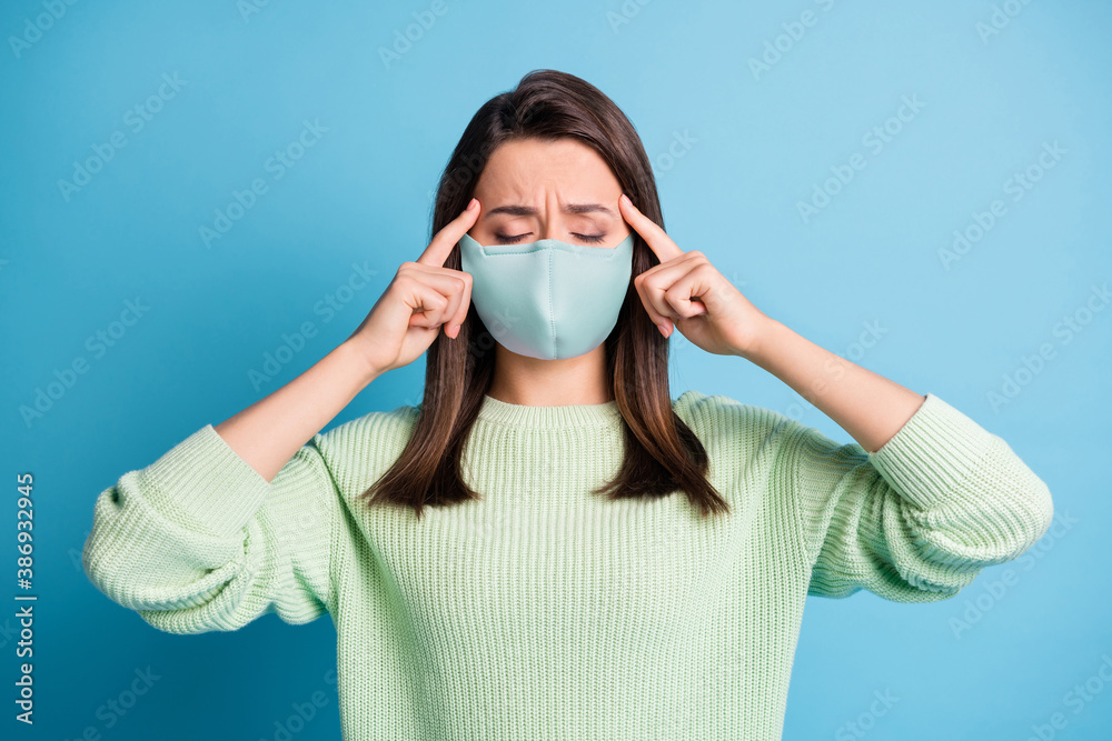 Photo of exhausted lovely girl eyes closed fingers head frown wear blue fabric face mask isolated blue color background Photo of exhausted lovely girl eyes closed fingers head frown wear blue fabric face mask isolated blue color background