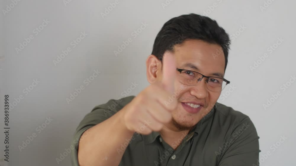 Portrait of young Asian man smiling to camera and showing thumbs up sign, good OK approving Portrait of young Asian man smiling to camera and showing thumbs up sign, good OK approving