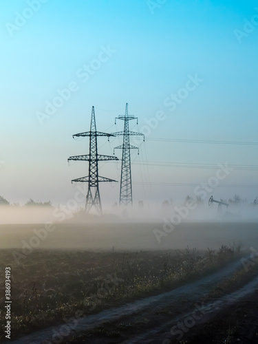 A foggy morning in an autumn field with a power line and a country road