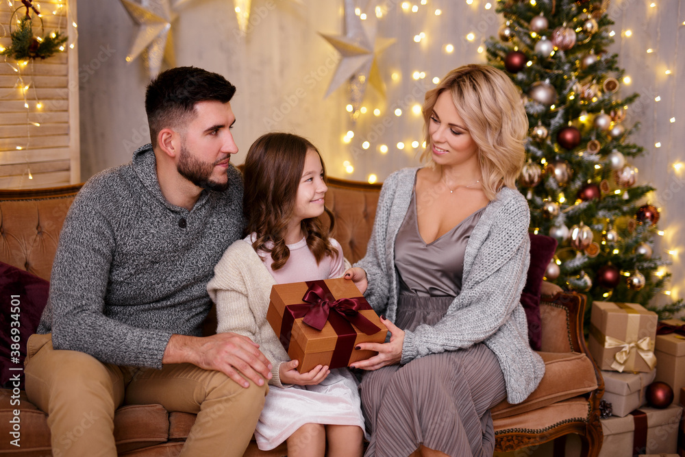 parents giving present to their daughter in living room with decorated Christmas tree